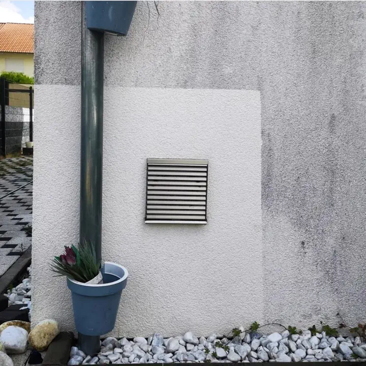Probefläche neben Fallrohr und Lüftungsgitter auf einer grau vergrauten Wand